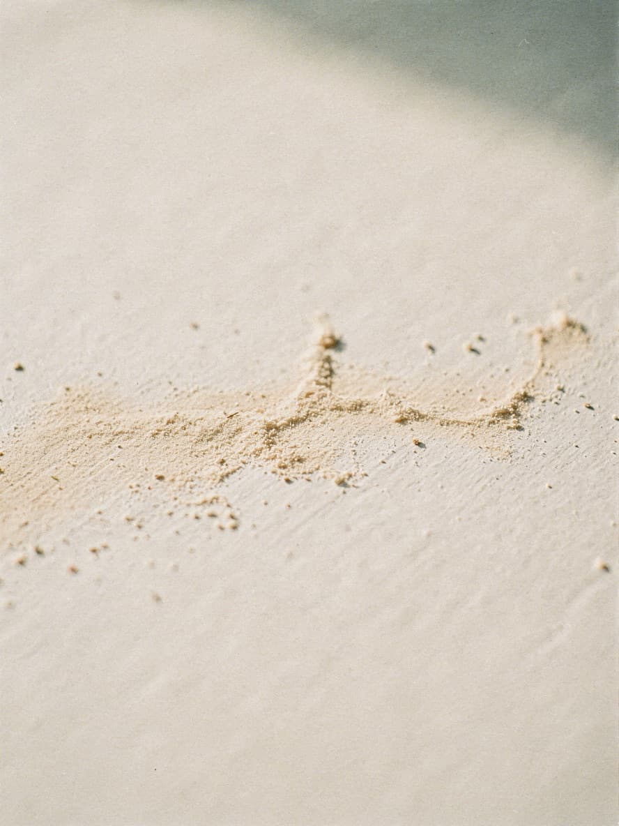 A scattered line of fine ochre powder drifting across a pale matte surface